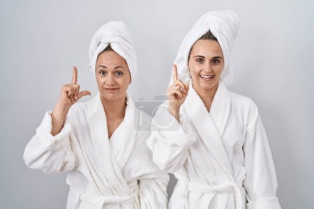 Téléchargez les photos : Middle age woman and daughter wearing white bathrobe and towel pointing finger up with successful idea. exited and happy. number one. - en image libre de droit