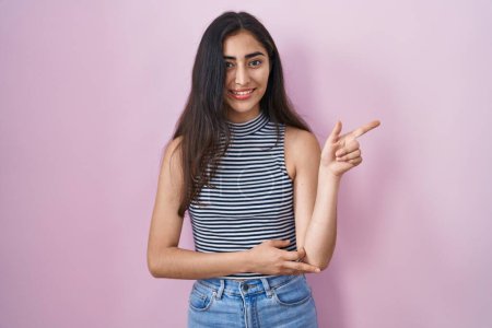 Foto de Young teenager girl wearing casual striped t shirt with a big smile on face, pointing with hand and finger to the side looking at the camera. - Imagen libre de derechos