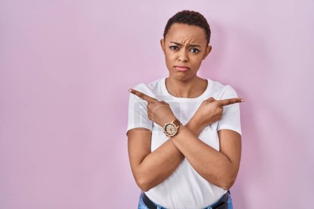 Foto de Beautiful african american woman standing over pink background pointing to both sides with fingers, different direction disagree - Imagen libre de derechos