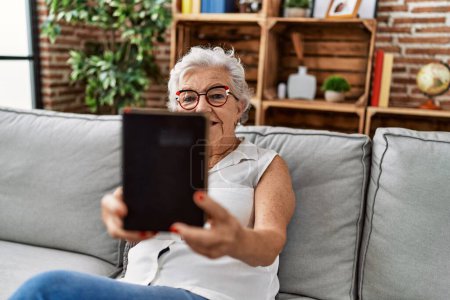 Téléchargez les photos : Femme âgée aux cheveux gris tenant une bible assise sur un canapé à la maison - en image libre de droit