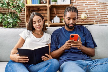 Photo for Man and woman couple using smartphone and reading book at home - Royalty Free Image