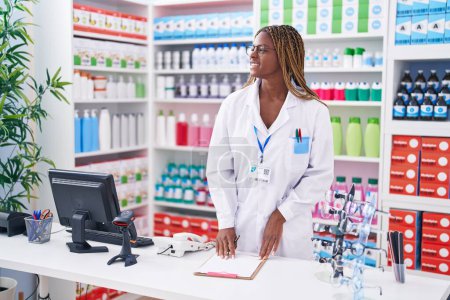 Téléchargez les photos : African american woman pharmacist smiling confident writing on document at pharmacy - en image libre de droit