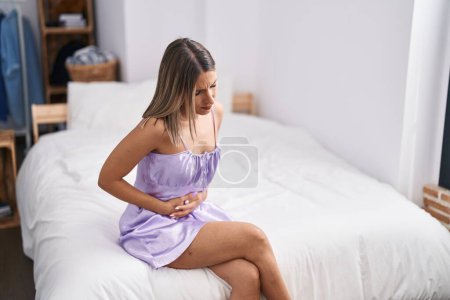 Photo for Young beautiful hispanic woman suffering for menstrual pain sitting on bed at bedroom - Royalty Free Image