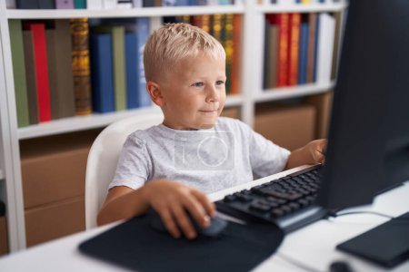 Foto de Adorable estudiante de niños pequeños usando computadora sentada en la mesa en el aula - Imagen libre de derechos