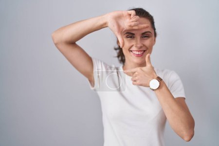 Téléchargez les photos : Beautiful brunette woman standing over isolated background smiling making frame with hands and fingers with happy face. creativity and photography concept. - en image libre de droit