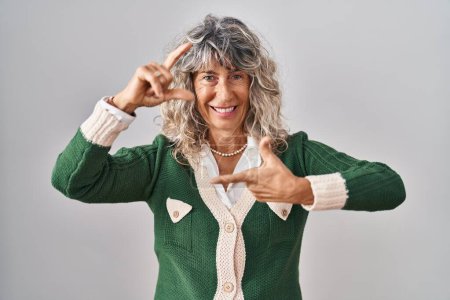 Téléchargez les photos : Middle age woman standing over white background smiling making frame with hands and fingers with happy face. creativity and photography concept. - en image libre de droit