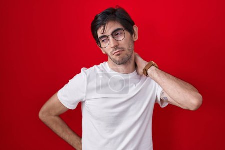 Téléchargez les photos : Young hispanic man standing over red background suffering of neck ache injury, touching neck with hand, muscular pain - en image libre de droit