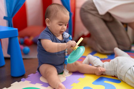Téléchargez les photos : Adorable bambin chinois jouant avec des jouets de plat et de fourchette assis sur le sol à la maternelle - en image libre de droit
