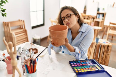 Photo for Young beautiful hispanic woman artist painting ceramic pot at art studio - Royalty Free Image