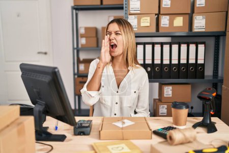 Téléchargez les photos : Young blonde woman working at small business ecommerce shouting and screaming loud to side with hand on mouth. communication concept. - en image libre de droit