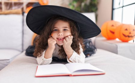 Foto de Adorable hispanic girl wearing halloween costume reading book at home - Imagen libre de derechos