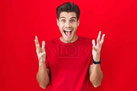 Photo for Young hispanic man standing over red background celebrating crazy and amazed for success with arms raised and open eyes screaming excited. winner concept - Royalty Free Image