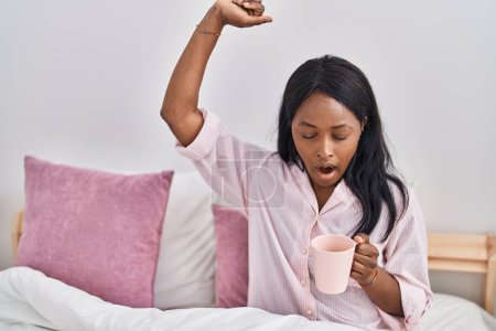 Photo for Young african american woman drinking coffee waking up at bedroom - Royalty Free Image
