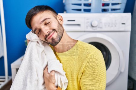 Photo for Young hispanic man smiling confident touching softener clothes with face at laundry room - Royalty Free Image