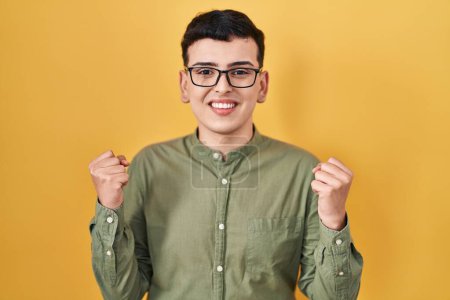 Foto de Non binary person standing over yellow background celebrating surprised and amazed for success with arms raised and open eyes. winner concept. - Imagen libre de derechos