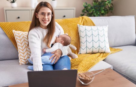 Téléchargez les photos : Mère et son fils en utilisant un ordinateur portable qui allaite bébé à la maison - en image libre de droit