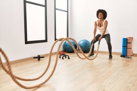 Photo for Young african american woman smiling confident training with battle rope at sport center - Royalty Free Image