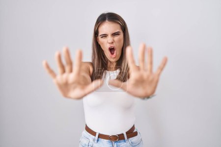 Foto de Hispanic young woman standing over white background doing stop gesture with hands palms, angry and frustration expression - Imagen libre de derechos