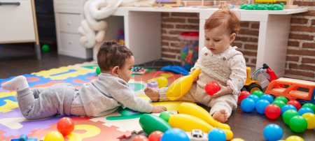 Photo for Two adorable babies playing with balls and bowling pin sitting on floor at kindergarten - Royalty Free Image