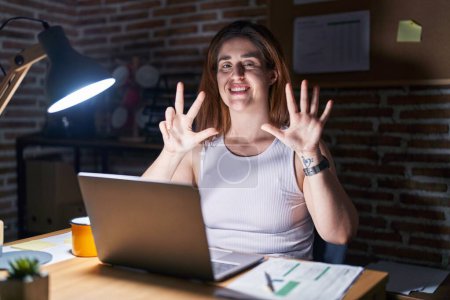 Téléchargez les photos : Brunette woman working at the office at night showing and pointing up with fingers number eight while smiling confident and happy. - en image libre de droit