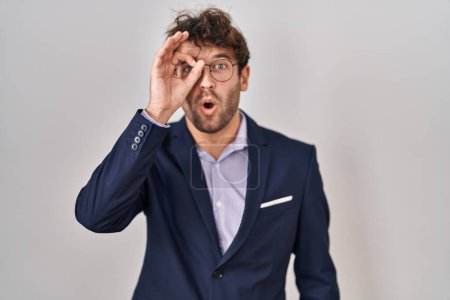 Photo for Hispanic business man wearing glasses doing ok gesture shocked with surprised face, eye looking through fingers. unbelieving expression. - Royalty Free Image