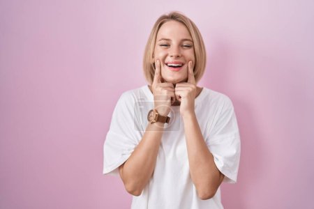 Photo for Young caucasian woman standing over pink background smiling with open mouth, fingers pointing and forcing cheerful smile - Royalty Free Image
