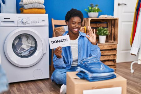 Téléchargez les photos : African american woman donating clothes doing ok sign with fingers, smiling friendly gesturing excellent symbol - en image libre de droit