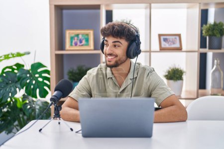 Téléchargez les photos : Homme arabe avec barbe travaillant à la radio regardant de côté avec le sourire sur le visage, expression naturelle. riant confiant. - en image libre de droit