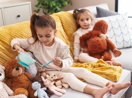 Téléchargez les photos : Deux enfants jouent avec des poupées assis sur le canapé à la maison - en image libre de droit