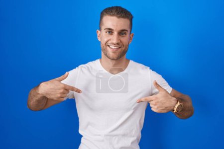 Photo for Young caucasian man standing over blue background looking confident with smile on face, pointing oneself with fingers proud and happy. - Royalty Free Image