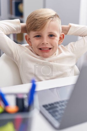 Téléchargez les photos : Adorable enfant en bas âge utilisant un ordinateur portable détendu sur la table en classe - en image libre de droit