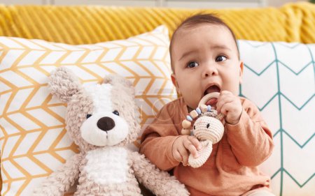 Foto de Adorable niño hispano mordiendo juguete sentado en el sofá en casa - Imagen libre de derechos