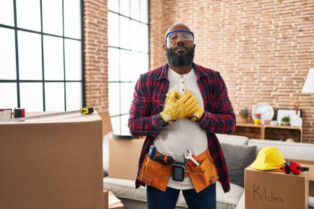 Foto de African american man working at home renovation smiling with hands on chest with closed eyes and grateful gesture on face. health concept. - Imagen libre de derechos