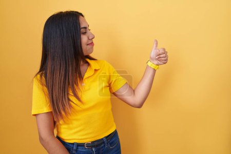 Téléchargez les photos : Young arab woman standing over yellow background looking proud, smiling doing thumbs up gesture to the side - en image libre de droit
