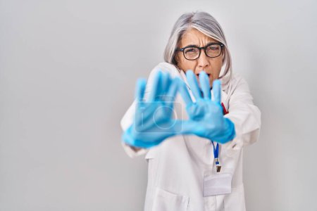 Photo for Middle age woman with grey hair wearing scientist robe afraid and terrified with fear expression stop gesture with hands, shouting in shock. panic concept. - Royalty Free Image