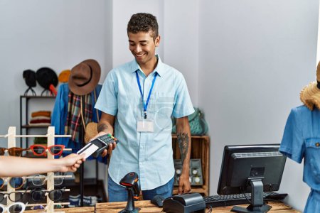Téléchargez les photos : Jeune homme hispanique travaillant comme assistant de magasin tenant dataphone au magasin de détail - en image libre de droit