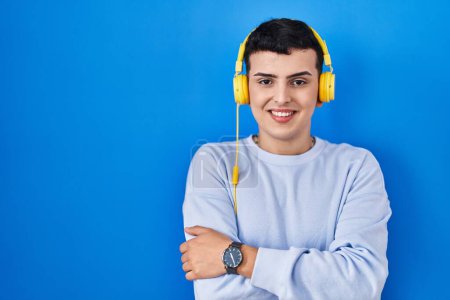 Téléchargez les photos : Non binary person listening to music using headphones happy face smiling with crossed arms looking at the camera. positive person. - en image libre de droit