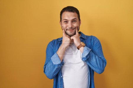 Téléchargez les photos : Hispanic man standing over yellow background smiling with open mouth, fingers pointing and forcing cheerful smile - en image libre de droit