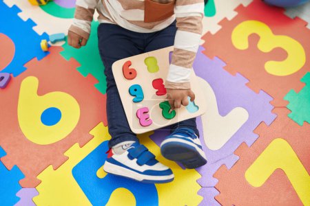 Téléchargez les photos : Adorable bambin hispanique jouer avec des mathématiques jeu de puzzle assis sur le sol à la maternelle - en image libre de droit