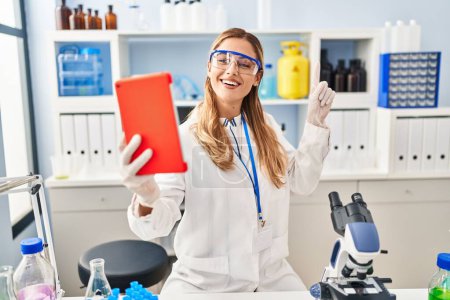 Téléchargez les photos : Young blonde scientist woman on video call working at laboratory smiling happy pointing with hand and finger to the side - en image libre de droit
