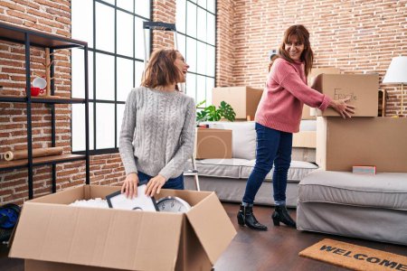 Photo for Two women mother and daughter unpacking cardboard box at new home - Royalty Free Image