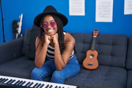 Foto de African american woman musician smiling confident sitting on sofa at music studio - Imagen libre de derechos
