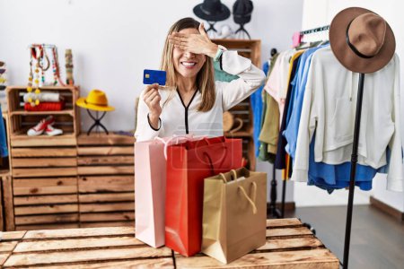 Photo for Young hispanic woman holding shopping bags and credit card at clothing store smiling and laughing with hand on face covering eyes for surprise. blind concept. - Royalty Free Image