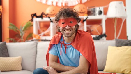 Foto de Young hispanic man wearing superhero costume having halloween party at home - Imagen libre de derechos