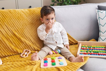 Téléchargez les photos : Adorable garçon hispanique jouant avec le jeu de mathématiques assis sur le canapé à la maison - en image libre de droit