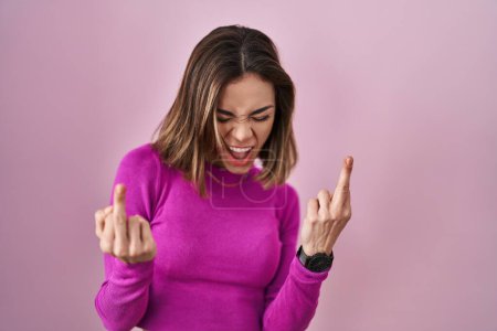Foto de Hispanic woman standing over pink background showing middle finger doing fuck you bad expression, provocation and rude attitude. screaming excited - Imagen libre de derechos