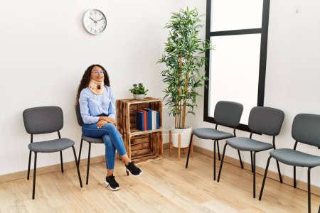 Photo for Young latin woman wearing neck collar sitting on chair at clinic waiting room - Royalty Free Image