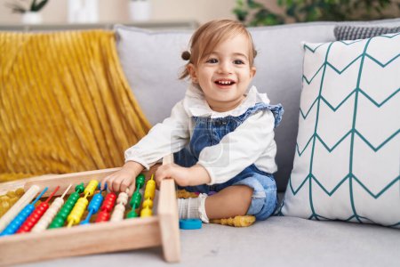 Photo for Adorable blonde toddler playing with abacus sitting on sofa at home - Royalty Free Image
