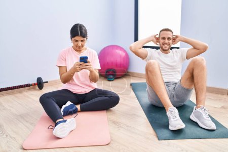 Photo for Man and woman couple smiling confident training abs exercise using smartphone at sport center - Royalty Free Image