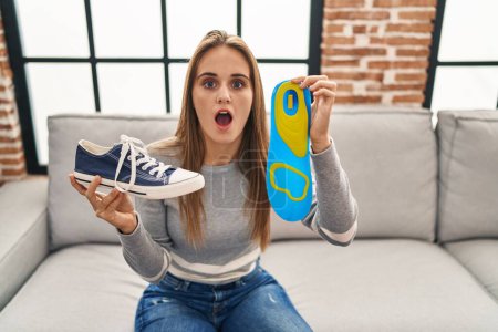 Photo for Young woman holding shoe insole afraid and shocked with surprise and amazed expression, fear and excited face. - Royalty Free Image